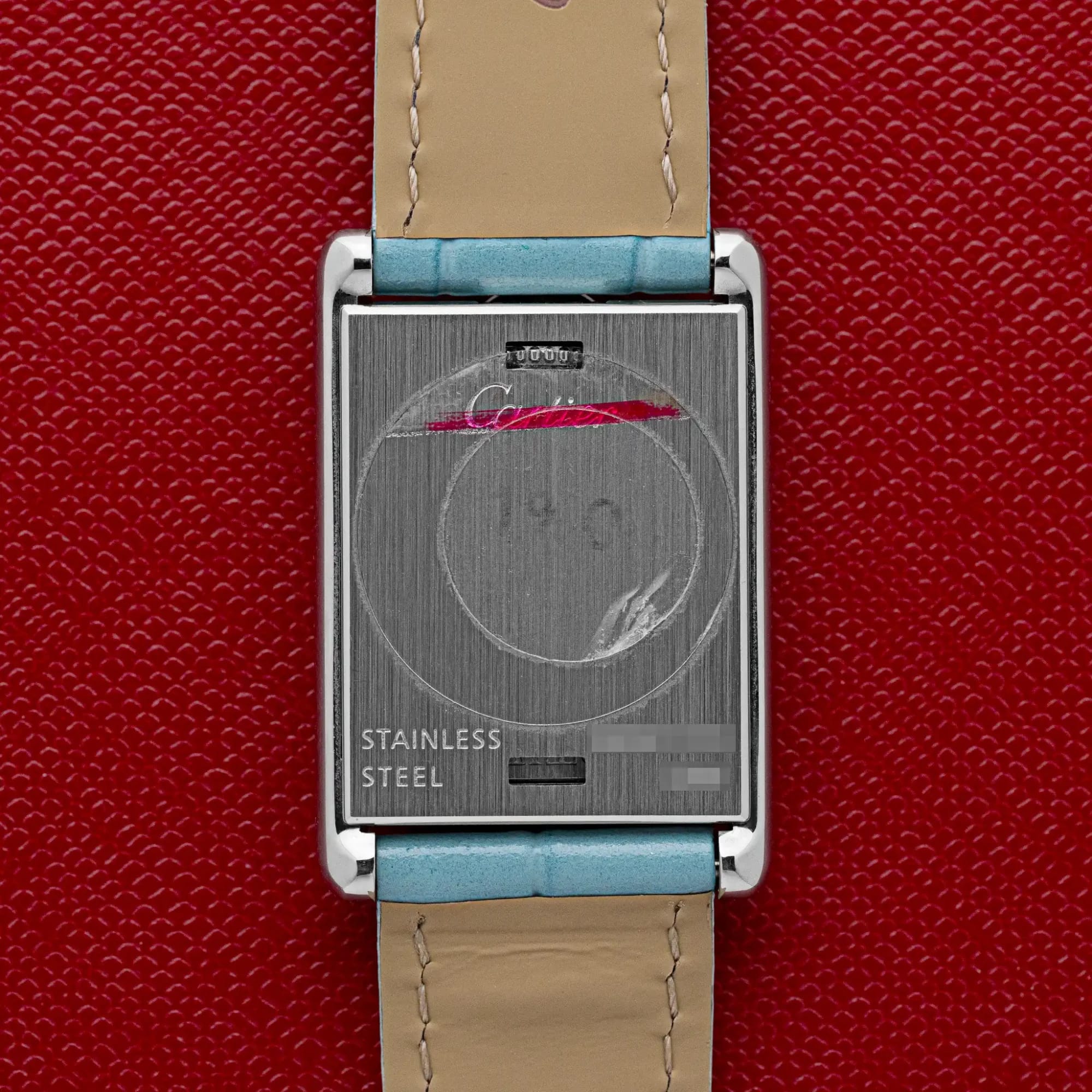 Steel case back of the Cartier Tank Basculante 2386 engraved "Stainless Steel" with Cartier signature, on a red background.