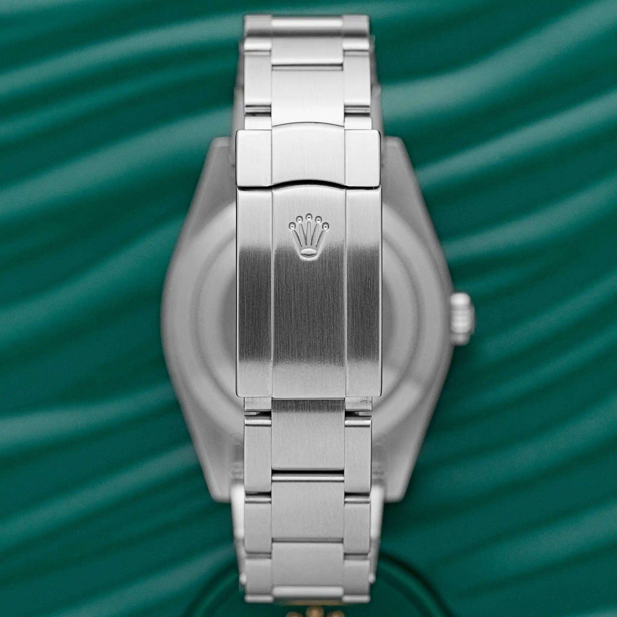 Rear view of the Rolex Oyster Perpetual 39 (114300) showing the steel Oyster bracelet and folding Oysterclasp engraved with the Rolex crown, on a green background.