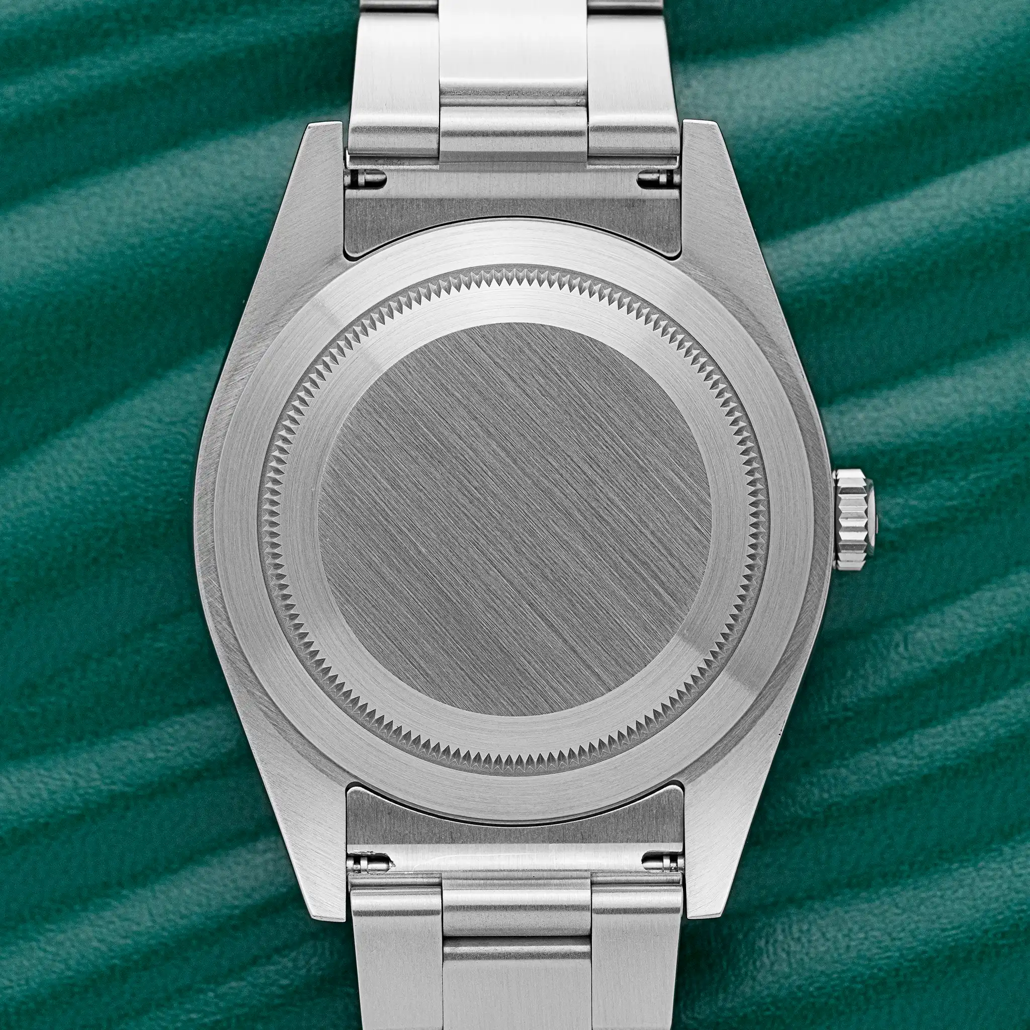 Rear view of the Rolex Oyster Perpetual 39 (114300) showing the smooth, polished steel screw-down caseback and steel Oyster bracelet, on a green background.