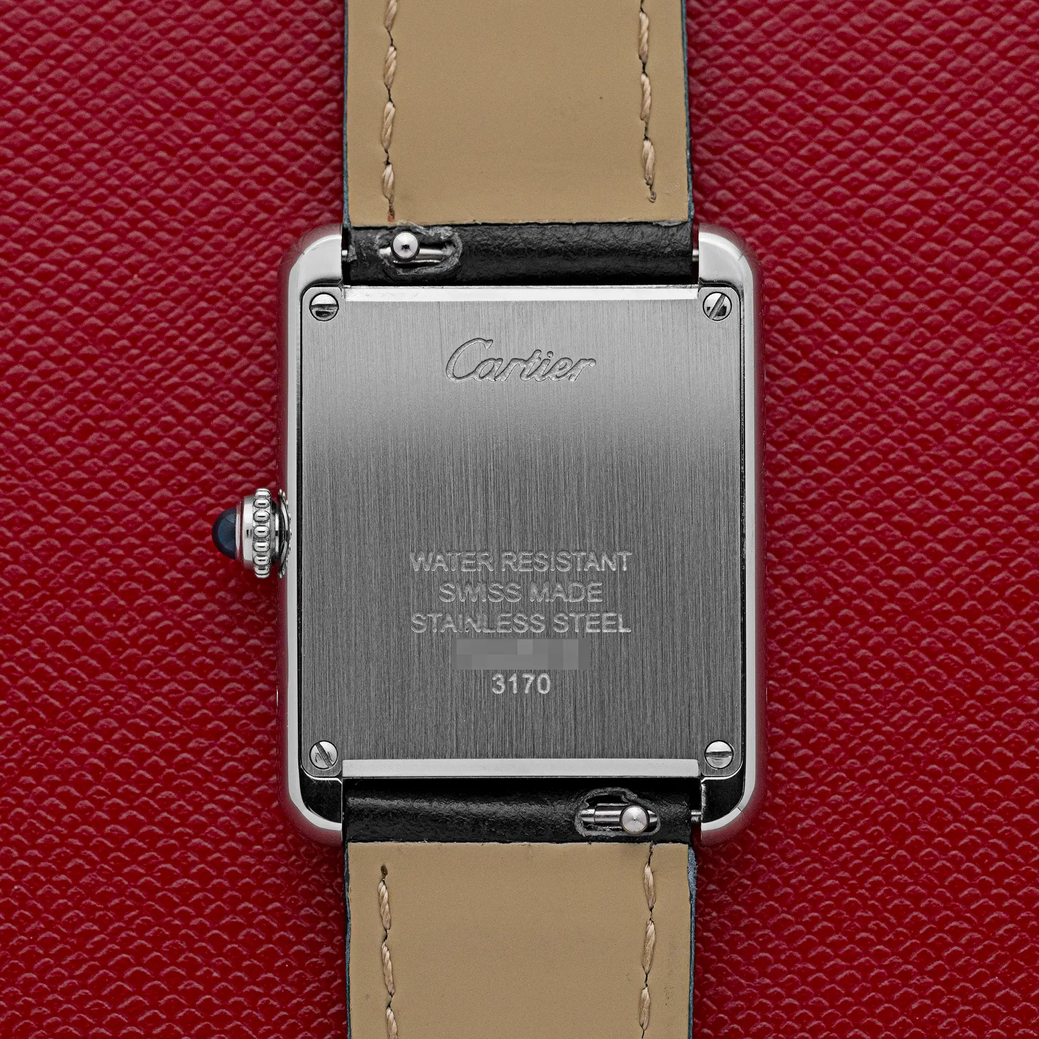 Steel caseback of the Cartier Tank Solo 3170 engraved "Cartier, Water Resistant, Swiss Made, Stainless Steel," on a red background.