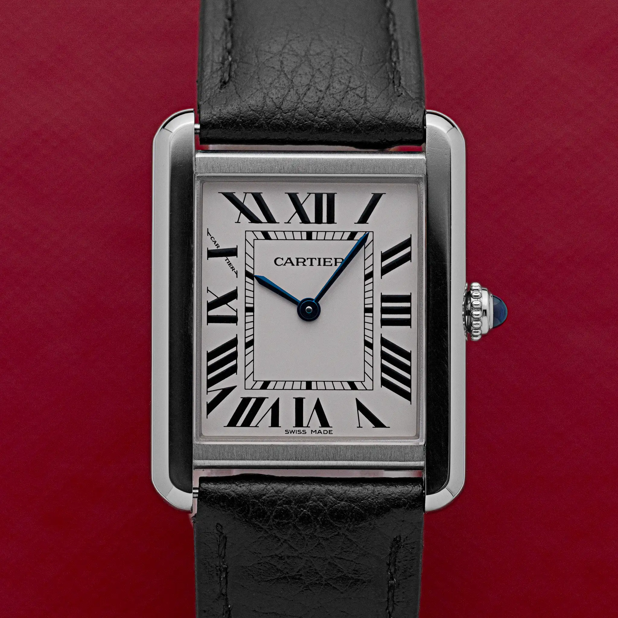 Front view of the Cartier Tank Solo 3170 with silver Roman numeral dial, blued hands, and blue cabochon crown, on a red background.