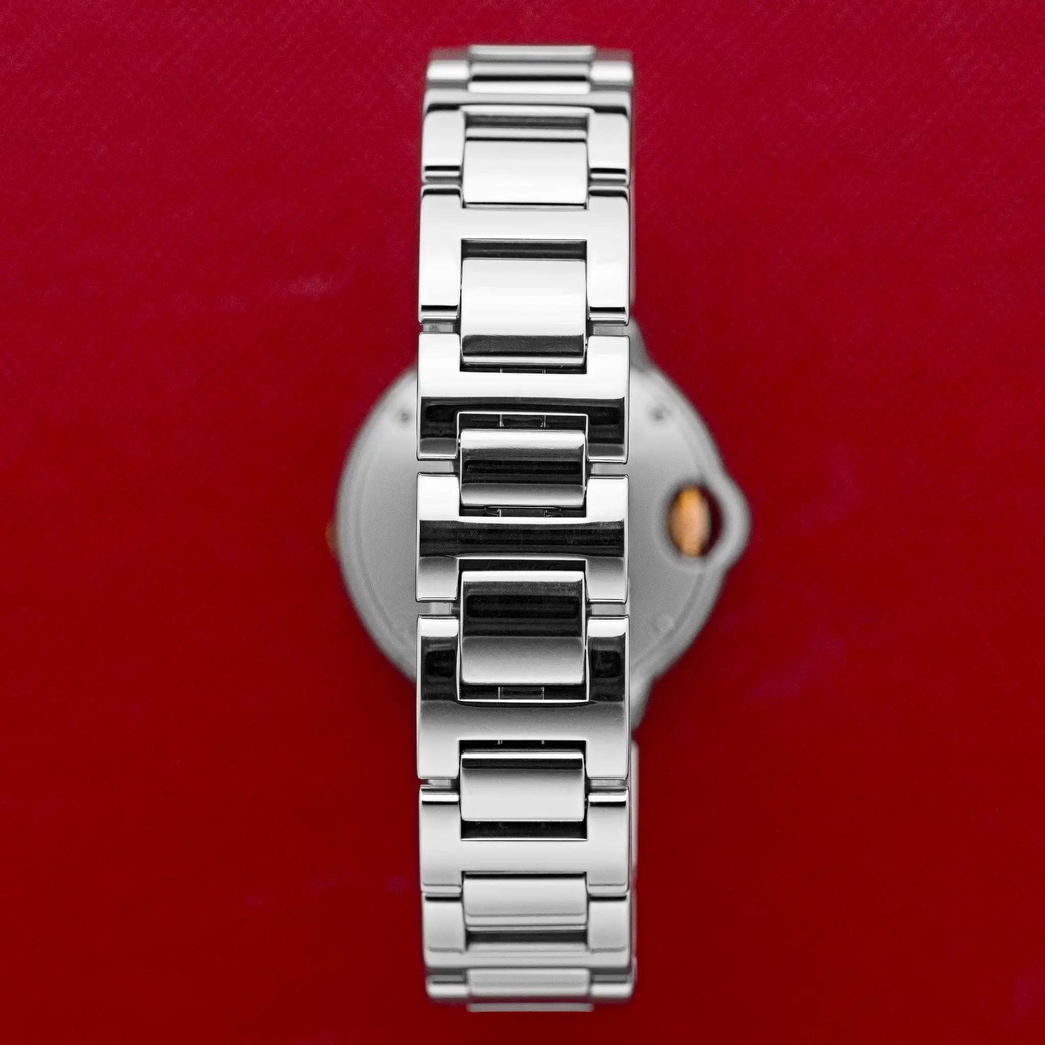 Close-up of the polished steel-and-rose-gold bracelet links of the Cartier Ballon Bleu 3009, on a red background.