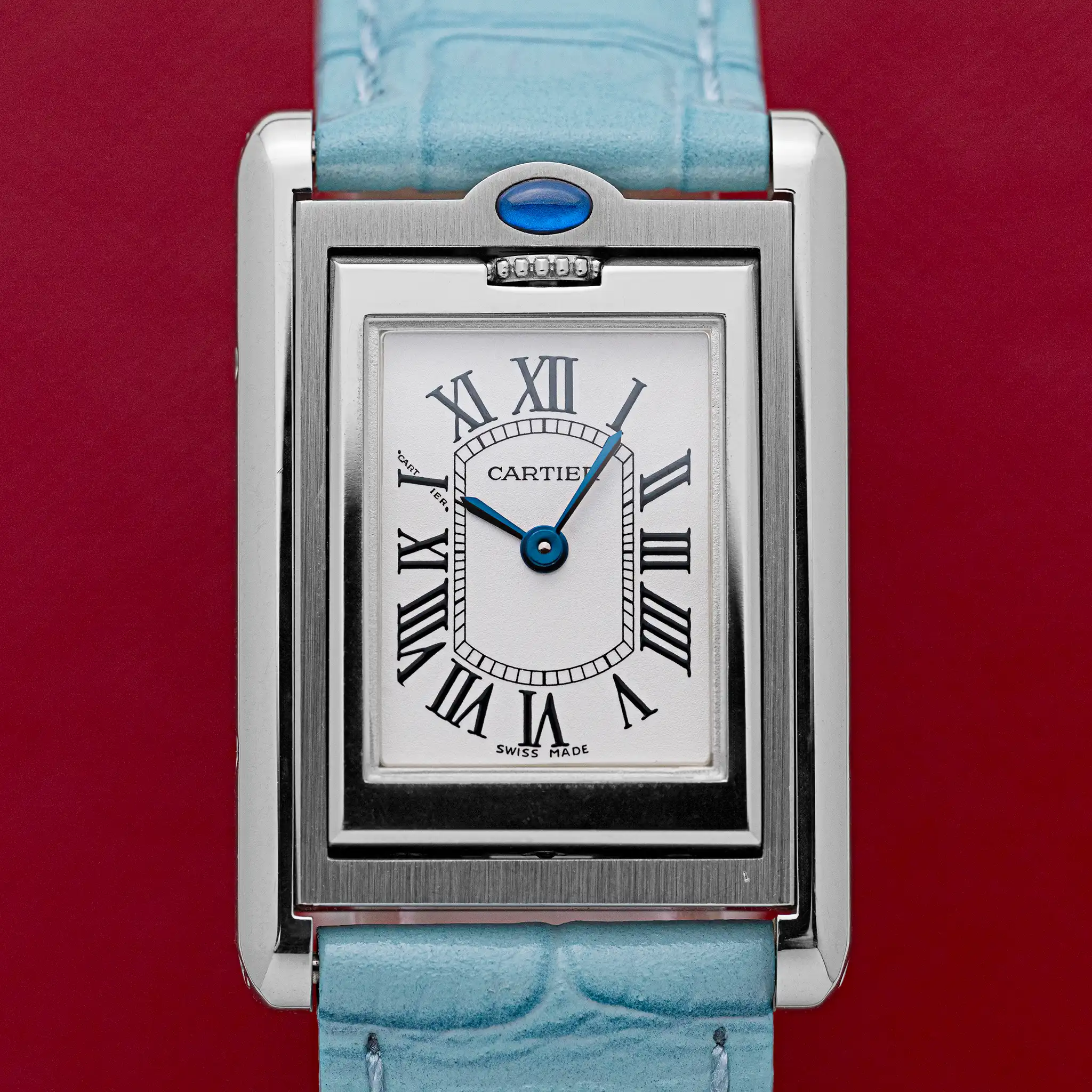 Light blue alligator strap of the Cartier Tank Basculante 2386 with polished steel pin buckle, on a red background.