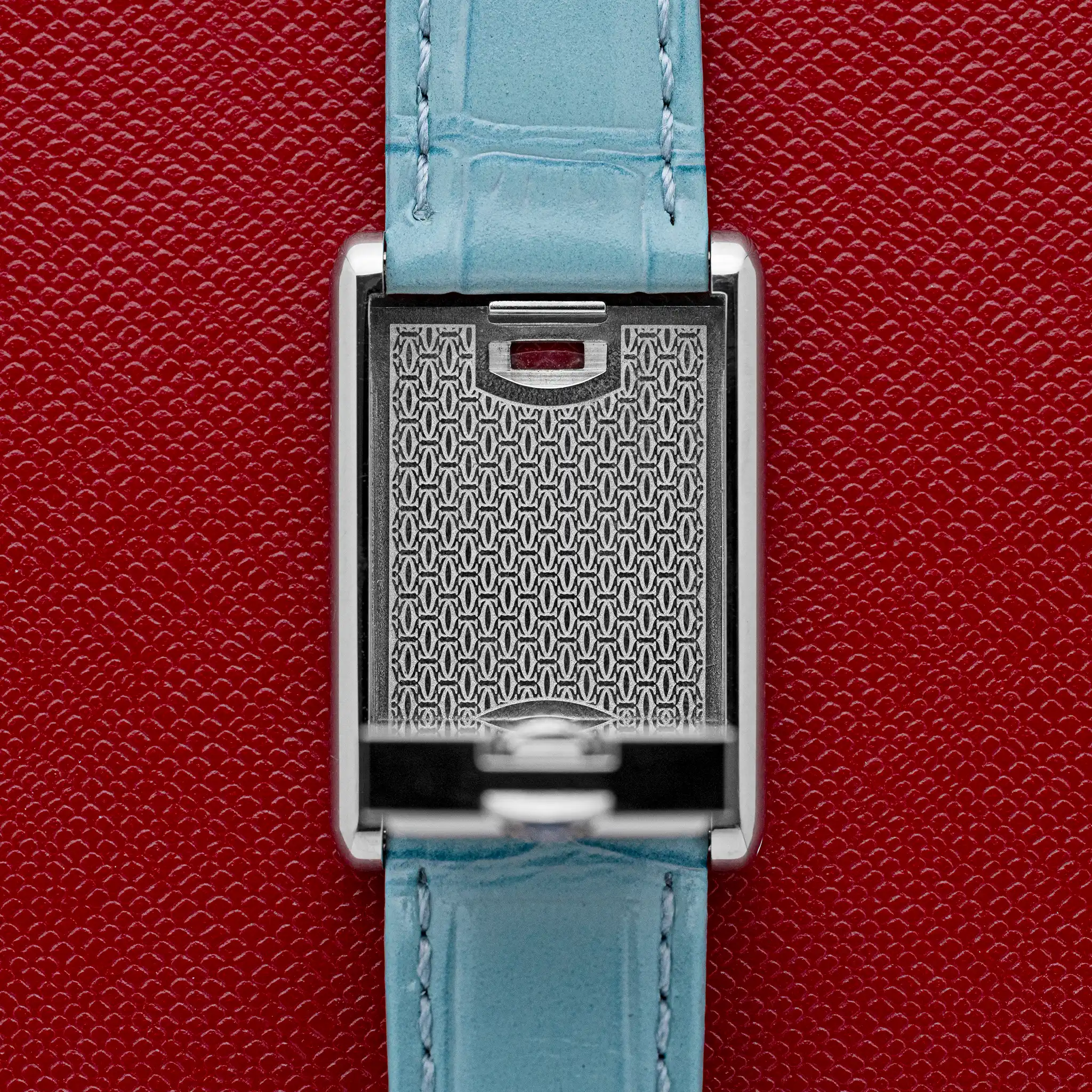 Inside of the Cartier Tank Basculante swivel cradle showing the engraved double-C monogram pattern, on a red background.